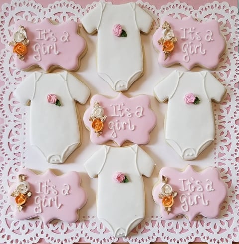 Decorated baby girl cookies with pink and white onesies and cloud shapes, adorned with floral details and text