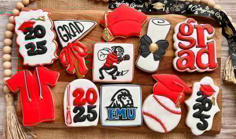 Decorative cookies arranged on a wooden surface featuring red and white graduate-themed designs with text and numbers