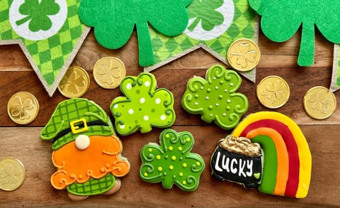 St. Patricks Day themed cookies and decorations on a wooden surface including leprechaun, shamrocks, pot of gold, and gold coins