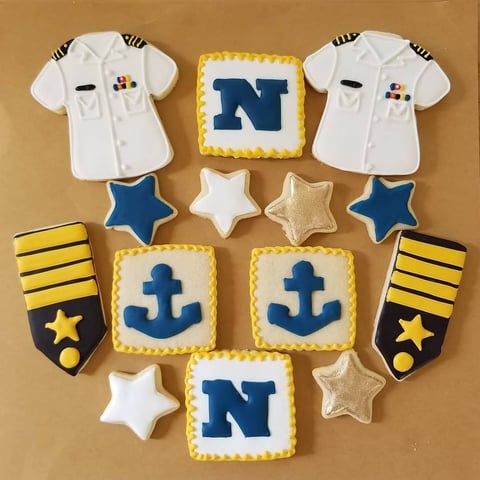 Nautical-themed decorated cookies and fondant navy uniforms arranged in a diamond pattern on tan background with baseball jersey, anchor, and star designs