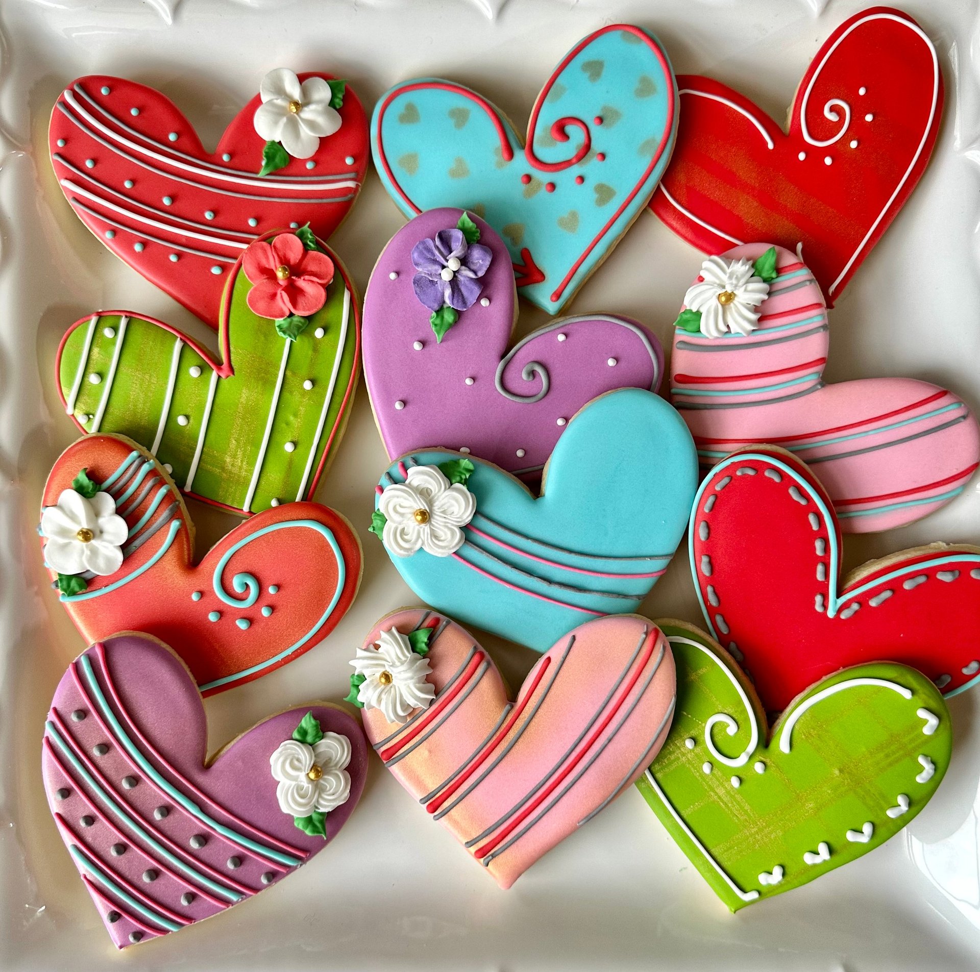 Colorful decorated heart-shaped cookies in red, pink, purple, blue, and green with striped icing and small fondant flowers