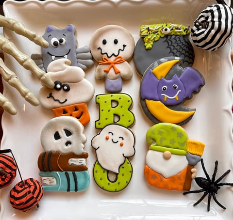 Decorated Halloween cookies including animals, ghosts, and monsters with colorful icing and embellishments arranged on a plate