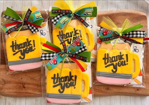 Decorated thank you cookies with yellow icing and pink trim on wooden boards, tied with colorful plaid ribbons and bows