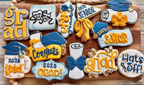 Decorative graduation-themed cookies featuring blue graduation caps, gold and white frosting, congratulatory text, and class year 2025 on wooden surface
